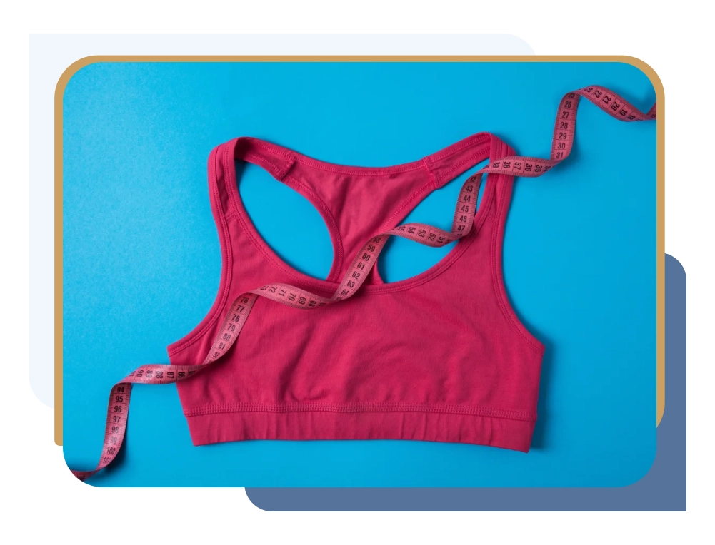 Elevated view of pink sports bra and measuring tape isolated on blue background
